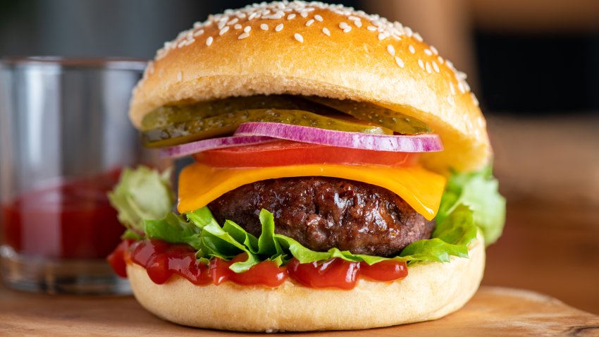 Homemade tasty freshly made burger with chips or french fries. Made from beef meat, cheese, salat leaves, tomatoes, onion, pickled cucumber and sauce